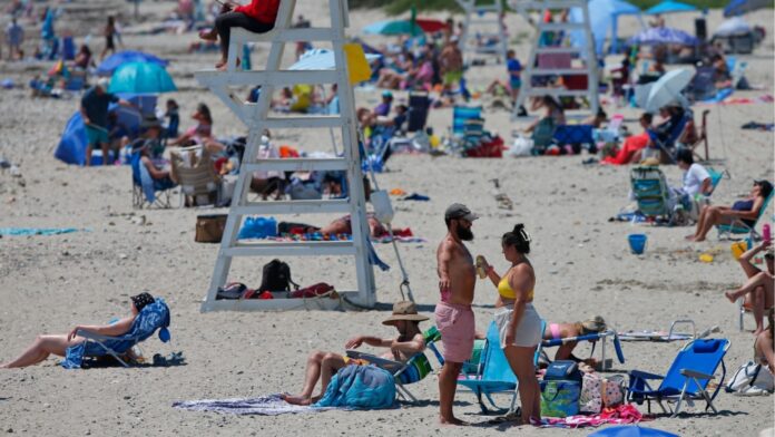 A woman sprays some sunscreen on a man at Horseneck Beach in Westport, Mass., on Tuesday, June 25, 2024 as temperatures continue to rise across the Northeast. (Peter Pereira/The Standard-Times via AP)